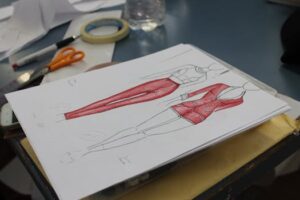 Close-up of fashion design sketches on a worktable with tools, showcasing red clothing designs.